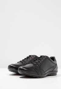 Pantofi negri din piele, cu o textură netedă, design cu șireturi, vârf rotund și talpă din cauciuc. Prezintă gauri metalice pentru șireturi și un branding subtil pe lateral.