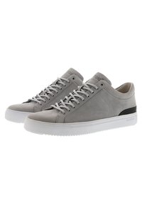 Zapatillas de ante gris con suelas de goma blanca, punta redonda y acentos en negro en el talón. Cuentan con cordones planos y ojetes para el cierre.