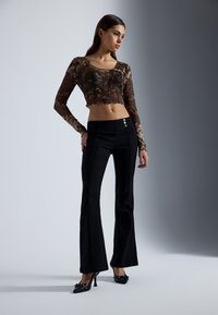 Black flared pants with a high waistband featuring silver buttons. The sheer brown floral long-sleeve top has a cropped design and ruffled hem.