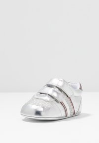 Silberner Babyschuh mit zwei Klettverschlüssen und Glitzerdetails, mit weißen und rosa Streifen an der Seite.