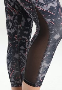 Legginsy z geometrycznym wzorem w czerni i szarości, z różowymi akcentami. Boczna część wykonana z czarnej siateczki dla lepszej wentylacji.