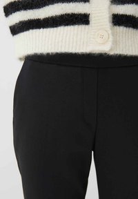 Zwarte op maat gemaakte broek van gladde stof, met een slim fit en zijzakken, gecombineerd met een crèmewitte en zwarte gestreepte trui met een knoop.