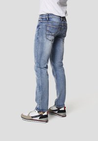 Lyseblå denimjeans med en slank pasform, fem lommer og diskret falmning. Kombineret med flerfarvede sneakers og en hvid t-shirt.
