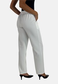 Witte op maat gemaakte broek met een elastische tailleband en zijzakken, met een gladde textuur en recht model. Draagt met zwarte hakken.