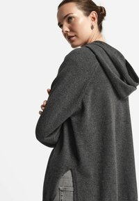 Kapuzenpullover in Anthrazitgrau aus weichem Stoff. Verfügt über einen lockeren Schnitt, seitliche Schlitze und eine glatte Textur.