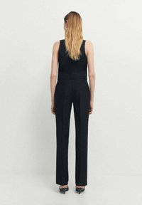 Čierny top bez rukávov v kombinácii s rovnými čiernymi nohavicami. Modelka stojí v priamej polohe, čím prezentuje čistý, minimalistický dizajn.