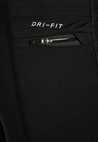 Czarna odzież sportowa z niewielką poziomą kieszonką na zamek błyskawiczny i białym napisem "DRI-FIT" nad kieszonką.