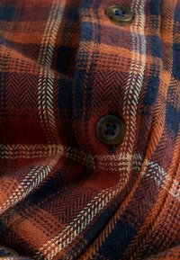 Flannel skjorte stof i orange, marineblå og creme ternet mønster. Har en struktureret vævning og brune knapper med "Superdry" gravering.