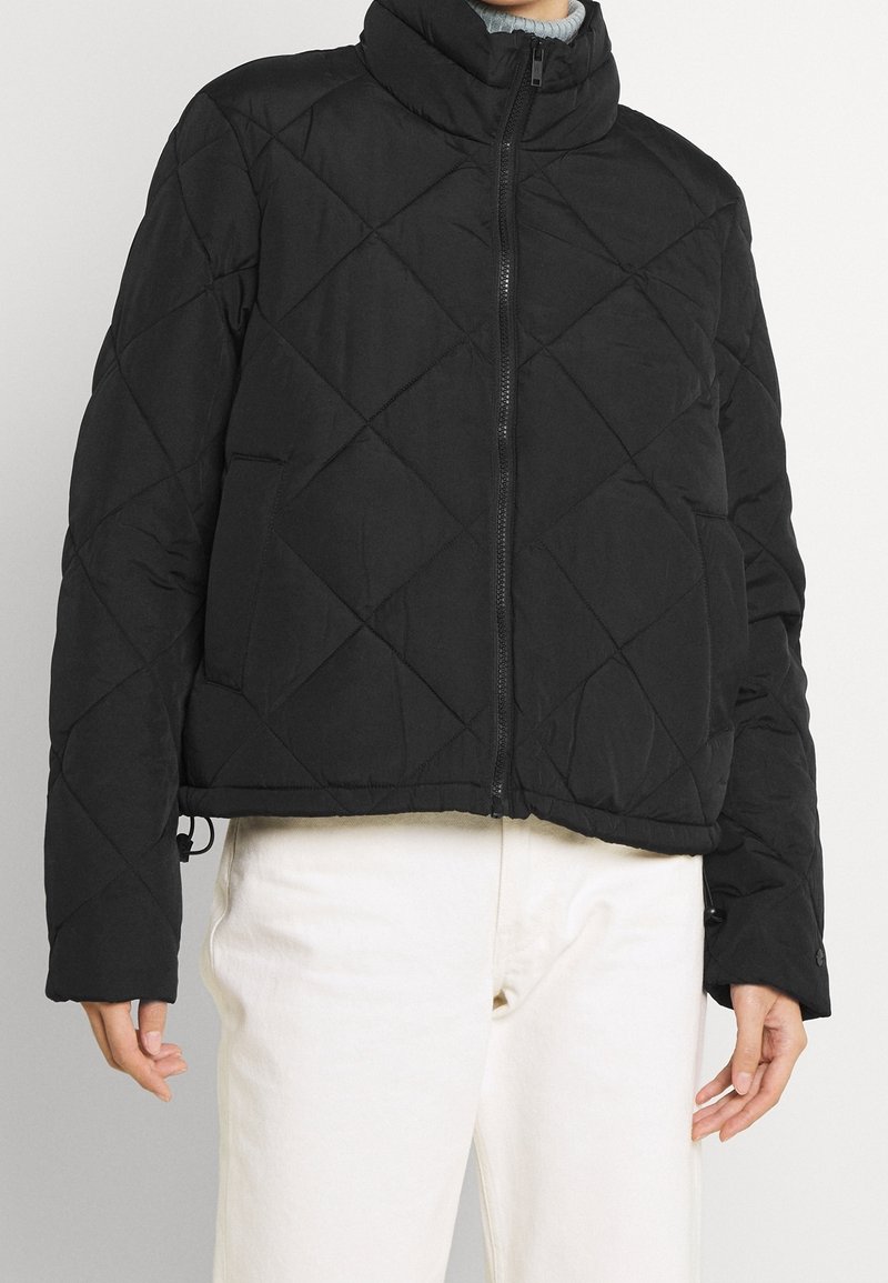 Sort quiltet pufferjakke med høj krave, cropped design, lynlåslukning foran og sidelommer; har en glat tekstur.
