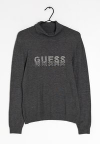 Grauer Strickpullover mit Rollkragen, auf der Vorderseite mit "GUESS" aus Strasssteinen verziert. Elastische Bündchen und Saum. Hängt an einem schwarzen Haken.