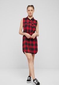 Vestito camicia a quadri rosso e nero con design senza maniche, due tasche sul petto, apertura frontale con bottoni e vita regolabile con lacci.