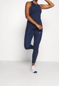 Marinblå sporttopp och leggings i stretchigt tyg, med nätpaneler och en liten Nike-logotyp, i kombination med vita träningsskor.