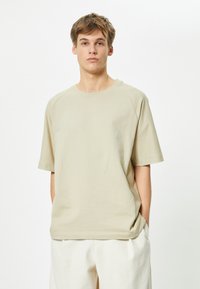 Väikebež t-särk lühikeste varrukatega, ümarama kaelusega ja raglan varrukatega, valmistatud pehmest puuvillaste materjalist, omades lõdvestatud lõiget ja minimaalset disaini.