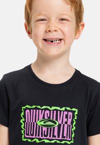 Camiseta negra de algodón con un gráfico colorido en tonos rosa y verde, y texto estilizado. Cuello redondo y mangas cortas.