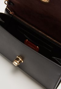 Czarna skórzana torebka z brązowym zamszowym wnętrzem, złotymi elementami, kieszenią na suwak i slotami na karty wewnątrz. Zamek zamykany jest metalowym zatrzaskiem.