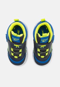 Scarpe sportive nere e blu con dettagli verde neon, tessuto testurizzato, cinturino regolabile e suola maculata, con una grafica di dinosauro.