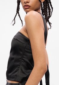 Top de cetim preto com um design ajustado, alças largas e um fecho lateral discreto. Textura suave e uma silhueta minimalista.