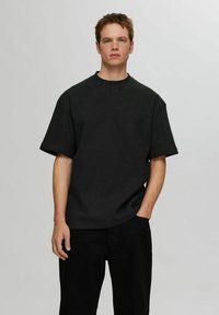 Svart våffelstickad kortärmad skjorta med avslappnad passform, ribbad rund halsringning och något sänkta axlar, matchad med svarta byxor.