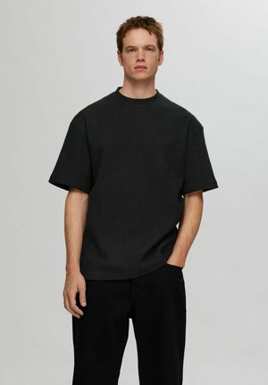 Zwart waffle-gebreid T-shirt met korte mouwen in een relaxte pasvorm, met een geribbelde ronde hals en iets verlaagde schouders, gecombineerd met zwarte broek.