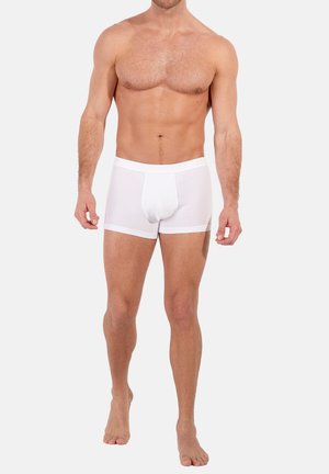 Boxer di cotone bianchi con una cintura morbida, design aderente e una tasca frontale per il supporto, indossati da un modello maschile in piedi.