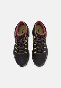 Scarpe da ginnastica nere con tomaia in rete, fodera bordeaux e dettagli verdi. Presentano una suola in gomma grigia e lacci scuri con dettagli riflettenti.