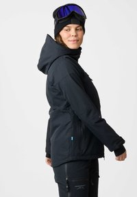 Black waterproof ski jacket with hood, zippered pockets, and blue accent. Worn with a black beanie and goggles featuring a blue lens.