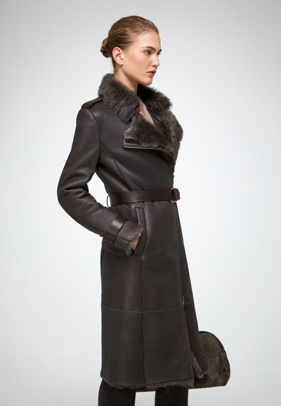 Manteau en cuir marron avec un col en fourrure, taille ceinturée, poches zippées et poignets doublés en fourrure. Texture lisse avec des détails de panneaux contrastants.