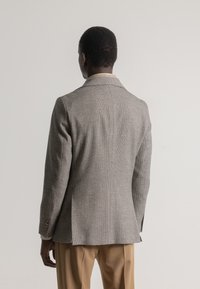 Blazer de espiga gris con solapas muesca, dos vents traseros y puños abotonados. Combinado con pantalones beige. Textura suave y tejida.