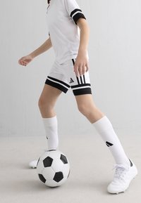 Biała koszulka piłkarska z czarnymi paskami, dopasowane spodenki z czarnymi akcentami, białe nagolenniki i białe korki. Obecna jest czarno-biała piłka do piłki nożnej.