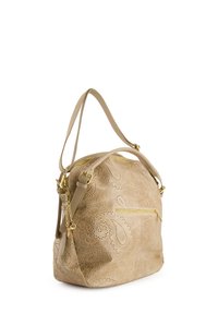 Tan håndtaske med dekorativ perforeret paisley-mønster, guldfarvede hardware-detaljer, dobbelt skulderstropper og en lynlåslomme på forsiden.