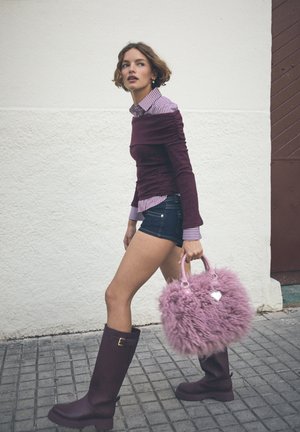 Burgundy tekstuuri tops, triibulise krae ja särgi all, teksashorts, põlvene ulatuvad burgundy saapad ja karvane roosa käekott südame ripatsiga.