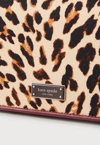 La borsa in tessuto con stampa leopardata presenta uno sfondo beige con macchie nere e marroni. Placca del logo in argento nella parte anteriore con la scritta "kate spade NEW YORK."