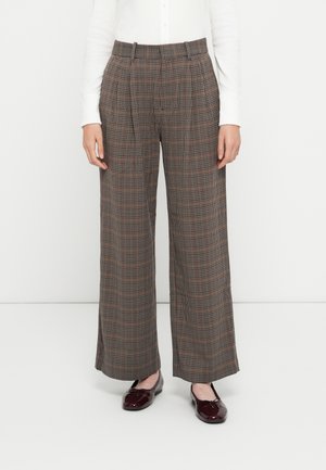 Bredde bukser i brunt rutemønster. Laget av myk stoff, med høy midje og legg, sammen med mørkerøde loafers.