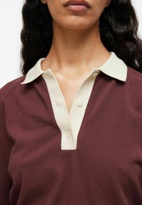 Bordeaux polo-shirt met een contrasterende beige kraag. Heeft een knoopsluiting met drie knopen en een textuurstof.