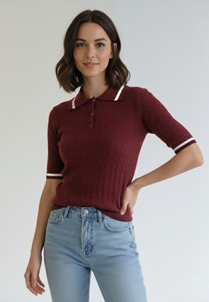 Bordowa dzianinowa koszulka polo z teksturowanym wzorem, białe rękawy z paskami i listwa z trzema guzikami. W zestawie z jasnoniebieskimi dżinsami.