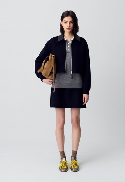 Chaqueta negra recortada con cuello de cuero, polo gris, falda gris, bolso de ante marrón, zapatillas plateadas y amarillas, calcetines color tostado.
