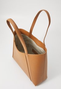 Sac cabas en cuir tan avec deux poignées allongées, ouverture en haut, et un intérieur doublé en tissu avec une poche zippée.