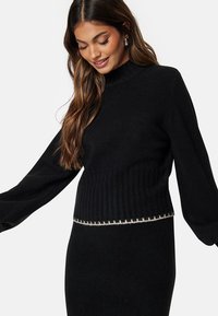 Maglione nero a coste con maniche lunghe, collo alto e orlo testurizzato caratterizzato da un dettaglio di cucitura in un colore chiaro a contrasto.