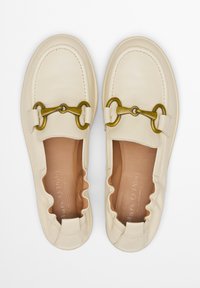 Crèmekleurige leren mocassinschoenen met een gegolfd ontwerp, voorzien van een goudkleurig hardwaredetail en een gladde afwerking aan de bovenkant.