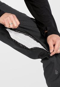Pantalons noirs avec poches latérales zippées, dotés d'un intérieur blanc avec de petits pois noirs. Matière texturée et athlétique avec un logo discret.