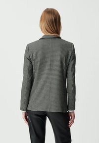 Marynarka w czarno-białą kratkę houndstooth o dopasowanym kroju, z klapami i długimi rękawami, zestawiona z czarnymi spodniami.