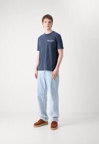 Marineblauwe katoenen t-shirt met 'New York' logo, gecombineerd met lichtblauwe denim jeans en bruine suede schoenen met tan zolen.
