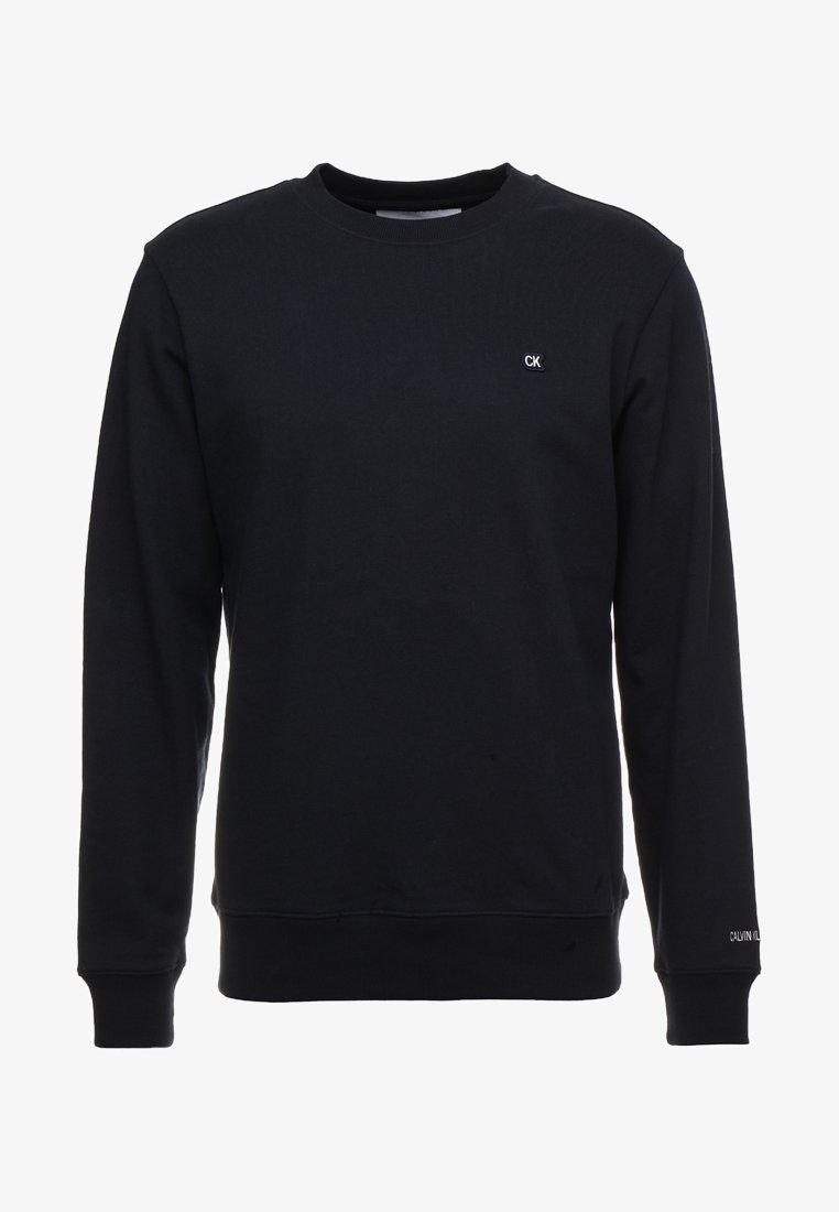 Sweat-shirt noir à manches longues avec col rond, petit logo CK sur la poitrine et texte Calvin Klein sur le poignet de la manche gauche.