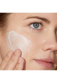 Nærbilde av et ansikt som påfører et kremaktig, hvitt hudpleieprodukt. Huden ser glatt og fuktet ut, med synlig tekstur og mykhet.
