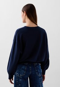 Mørkeblå oversized sweatshirt med rund halsudskæring og dropped shoulders, parret med højtaljede, slidte denim jeans med patch-lommer.
