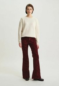 Pantalons évasés cramoisis en tissu texturé avec un motif floral, associés à un simple pull crème, souligné par un col rond et une coupe décontractée.