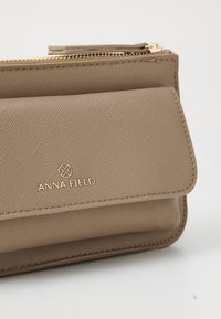 Béžová peněženka vyrobená z texturovaného syntetického materiálu, s zlatým zipem, překlopným klopou a embosovaným logem "ANNA FIELD".