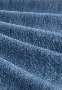 Denim tkanina u raznim nijansama plave, s teksturiranom površinom vidljivih uzoraka tkanja i suptilnim varijacijama boje.