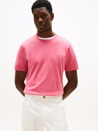 Ρόζ βαμβακερό T-shirt με στρογγυλή λαιμόκοψη, κοντά μανίκια και μικρό λογότυπο στο αριστερό στήθος. Συνδυασμένο με λευκά παντελόνια. Λείο υλικό.