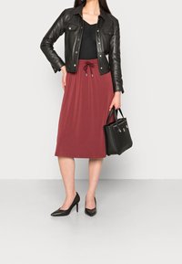 Veste en cuir noir sur un haut noir ajusté, associée à une jupe midi bordeaux avec taille élastique à cordon. Escarpins noirs et sac à main.